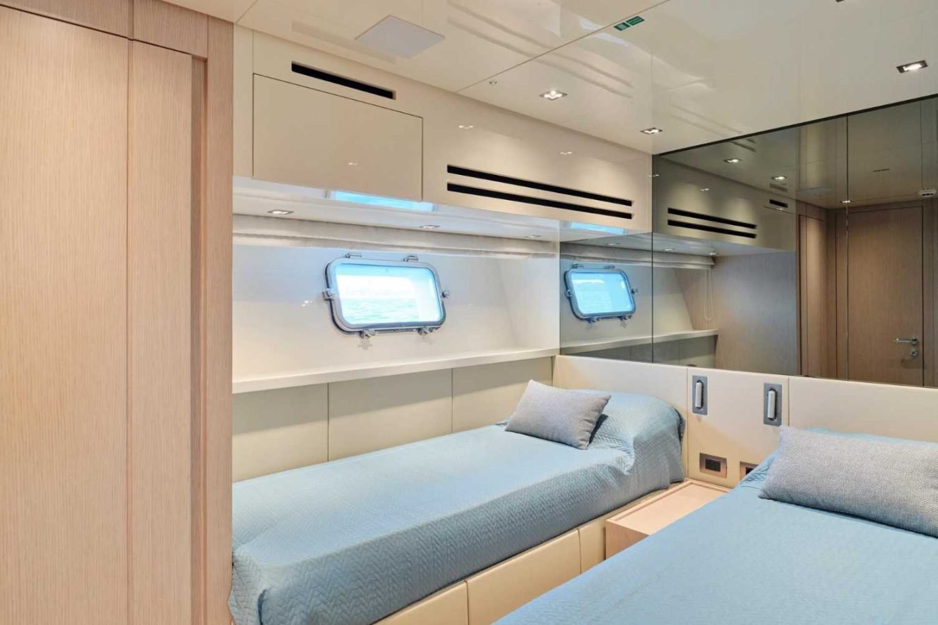Modern Sanlorenzo SX76 Fuquet Duet yacht cabin with two single beds, blue bedding, window, and minimalist wood accents.