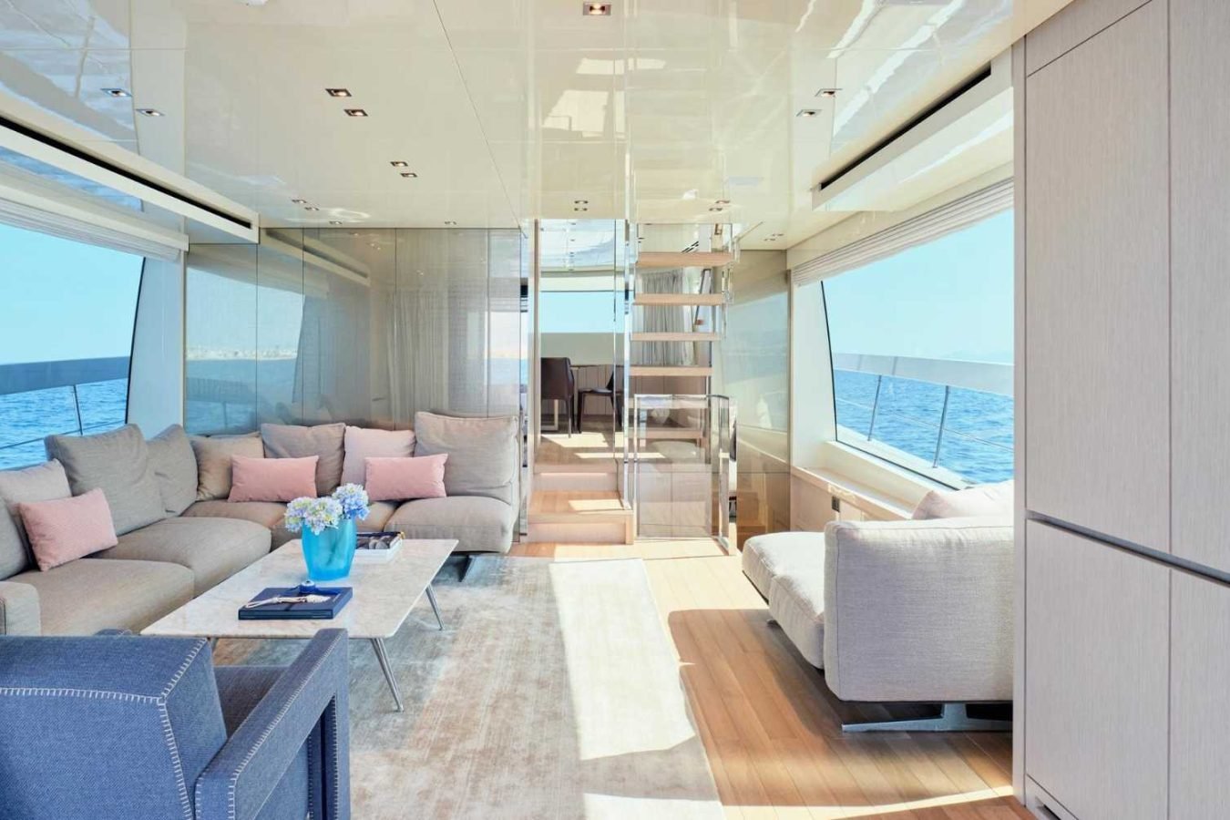 Modern Sanlorenzo SX76 Fuquet Duet yacht lounge with large windows, beige sofas, pink pillows, and ocean view.