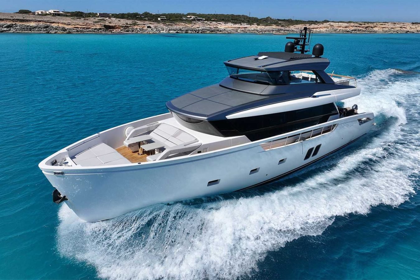The Sanlorenzo SX76 Fuquet Duet glides through turquoise water, leaving a foamy wake near the rocky shoreline.