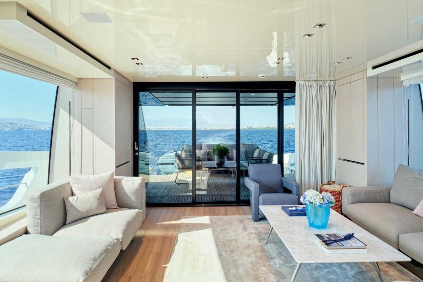 Modern Sanlorenzo SX76 Fuquet Duet yacht lounge with gray sofas, marble table, and large windows facing the ocean.