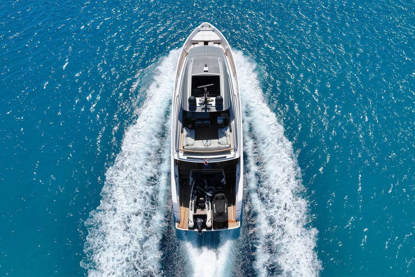 A Sanlorenzo SX76 Fuquet Duet motor yacht speeds across clear blue water, leaving white wake trails behind.