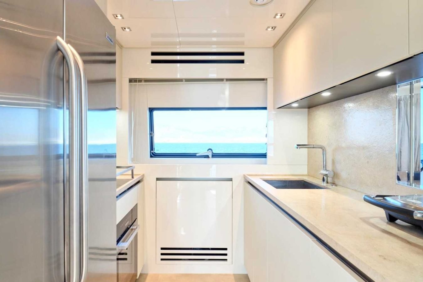 Bright modern galley kitchen on Sanlorenzo SX76 Fuquet Duet yacht, with white cabinets, ocean view, and stainless fridge.
