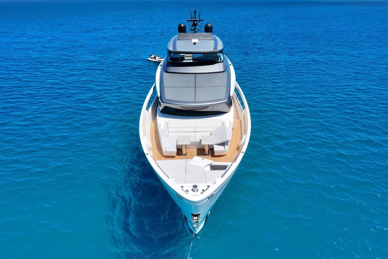 A Sanlorenzo SX76 Fuquet Duet yacht sits anchored in calm, clear blue water under a sunny sky, viewed from the front.