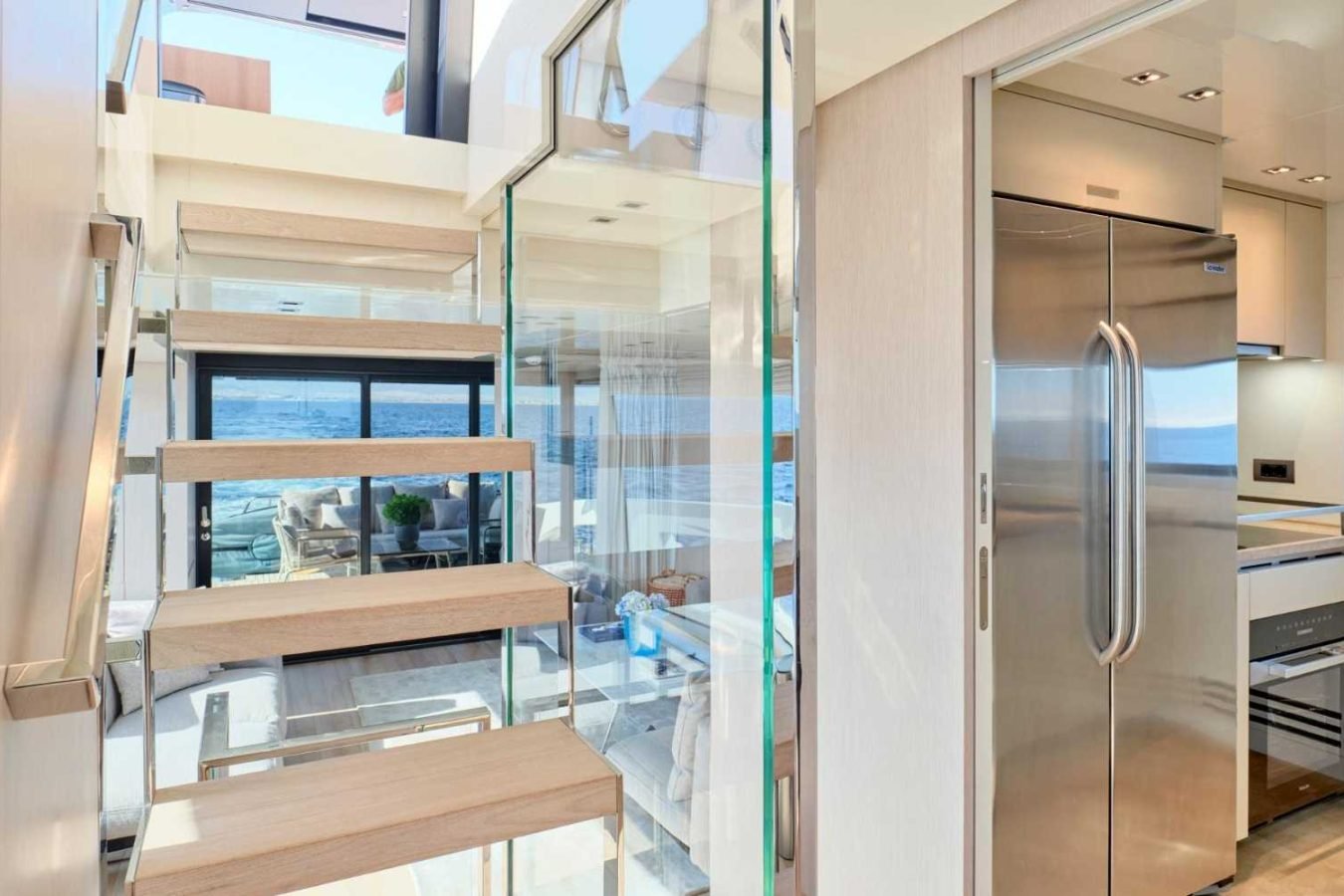 Modern kitchen on Sanlorenzo SX76 Fuquet Duet, stainless fridge, glass rail stairs, and ocean view through bright windows.