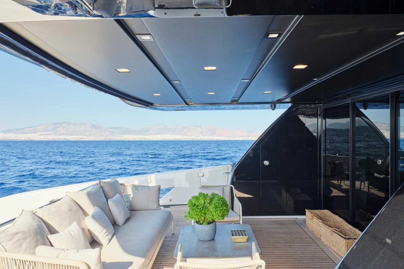 Modern Sanlorenzo SX76 Fuquet Duet yacht deck with cushioned seating, potted plant, and ocean view under shaded ceiling.