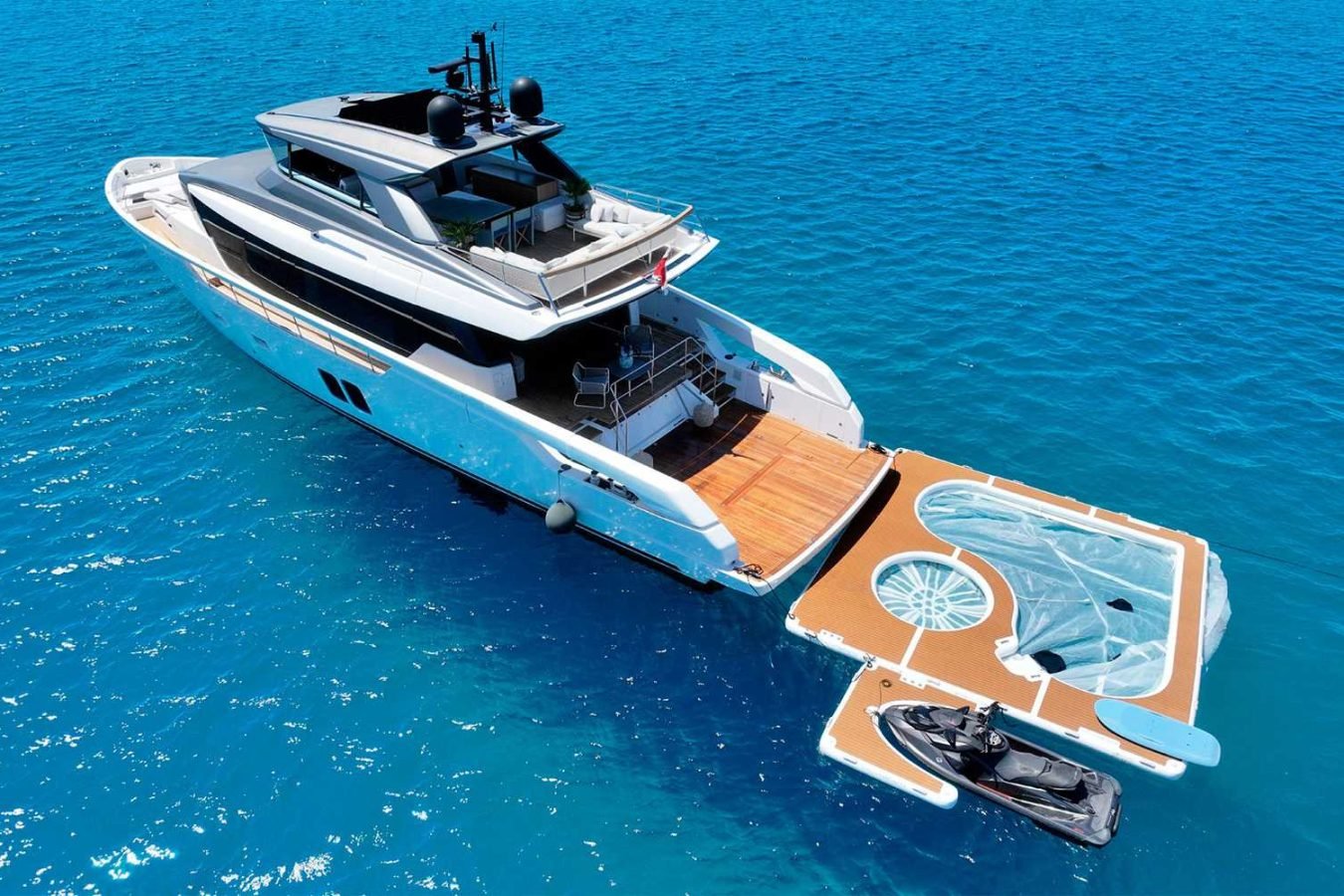 The Sanlorenzo SX76 Fuquet Duet luxury yacht floats on blue sea with a swim platform, jet ski, and inflatable lounge.