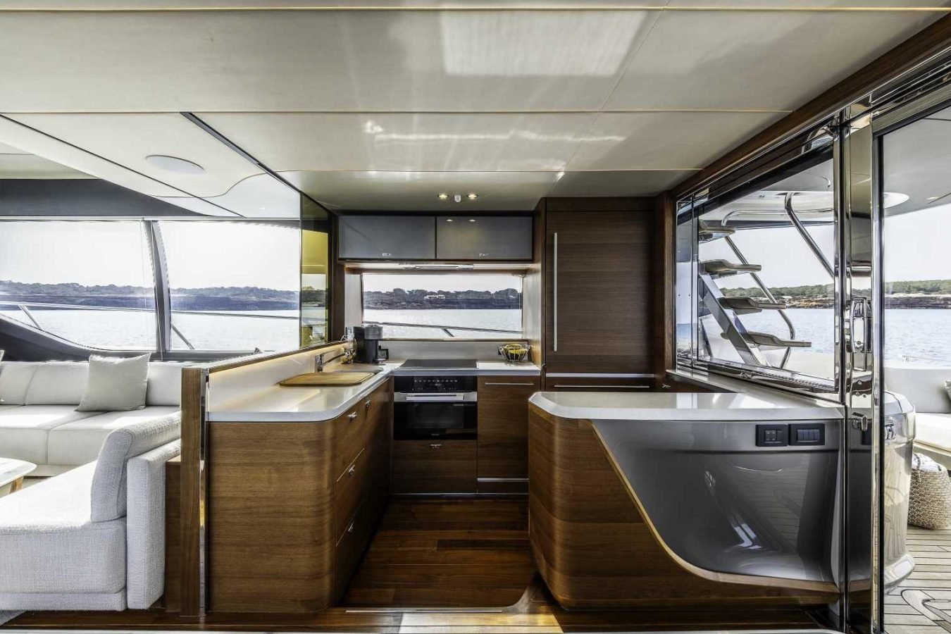Modern Princess S78 yacht kitchen with wood cabinets, white countertops, and large windows overlooking the shoreline.