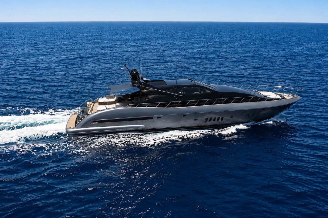 A sleek Mangusta 105 cruises swiftly across deep blue waters under a clear, sunny sky—perfect for a yacht charter.