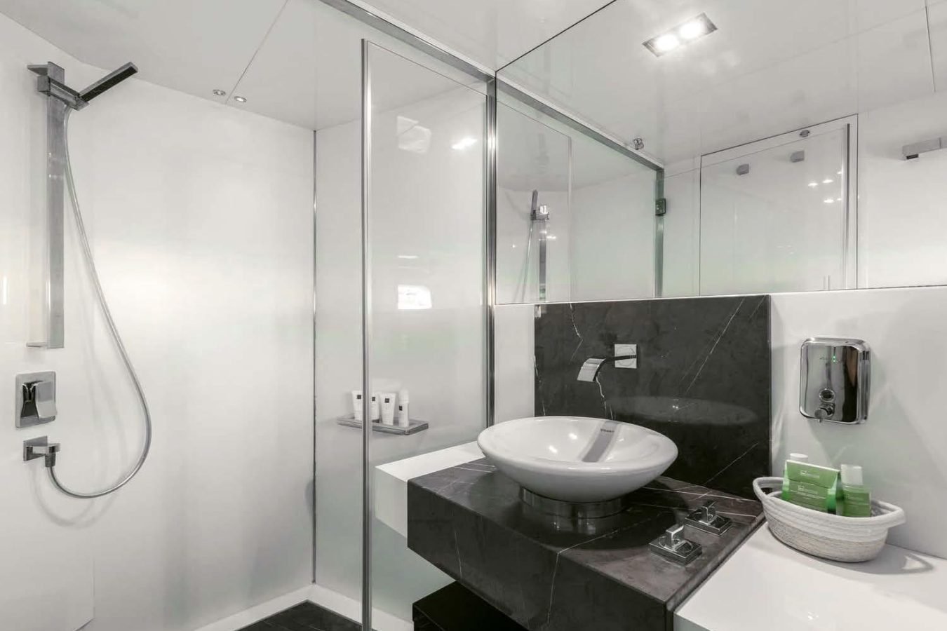 Modern white bathroom on Arcadia 85 yacht for charter, with vessel sink, glass shower, and amenities basket by the sink.