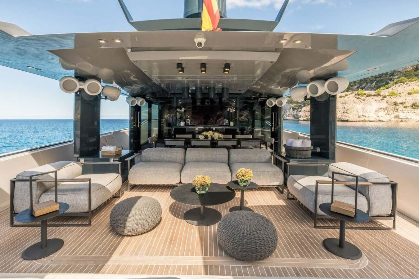 Luxurious Arcadia 85 yacht for charter: modern gray seating, round tables, sea view, under large canopy with speakers.