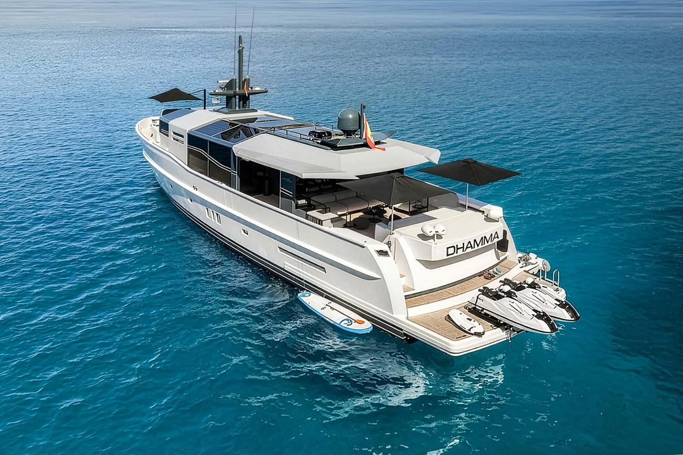 The luxury Arcadia 85 yacht for charter, DHAMMA II, floats on clear blue water with jet skis and a paddleboard at the stern.