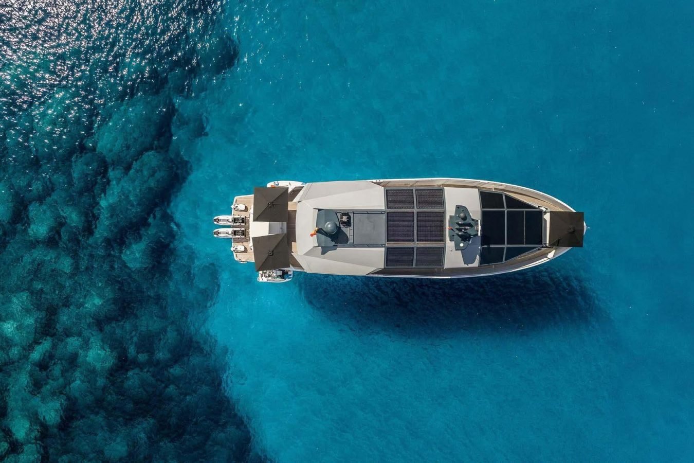 Aerial view of the Arcadia 85 yacht Dhamma II with solar panels, floating on clear blue water near a reef.