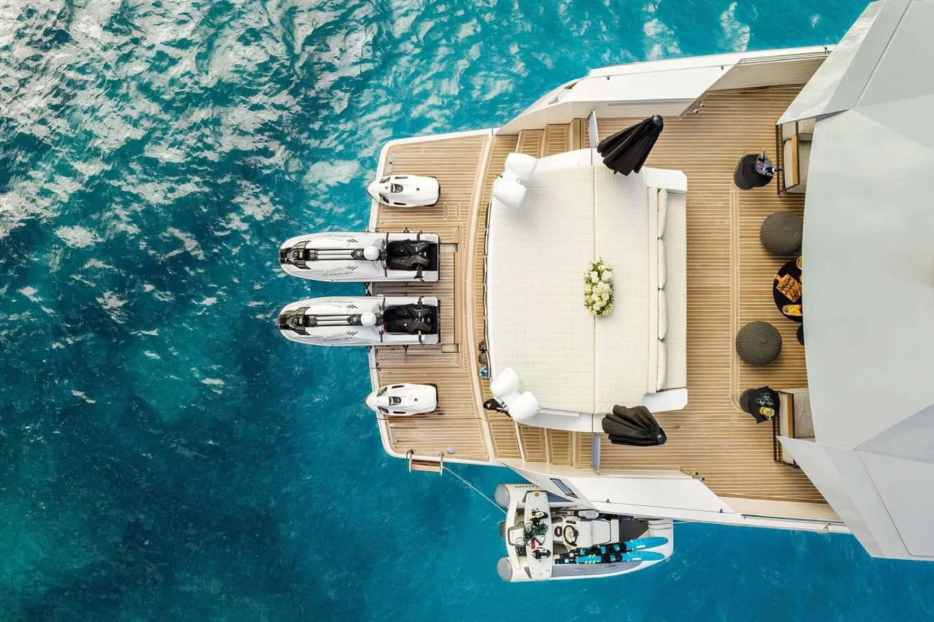 Aerial view of Arcadia 85 yacht for charter with deck seating, jet skis, and people relaxing on blue ocean water.