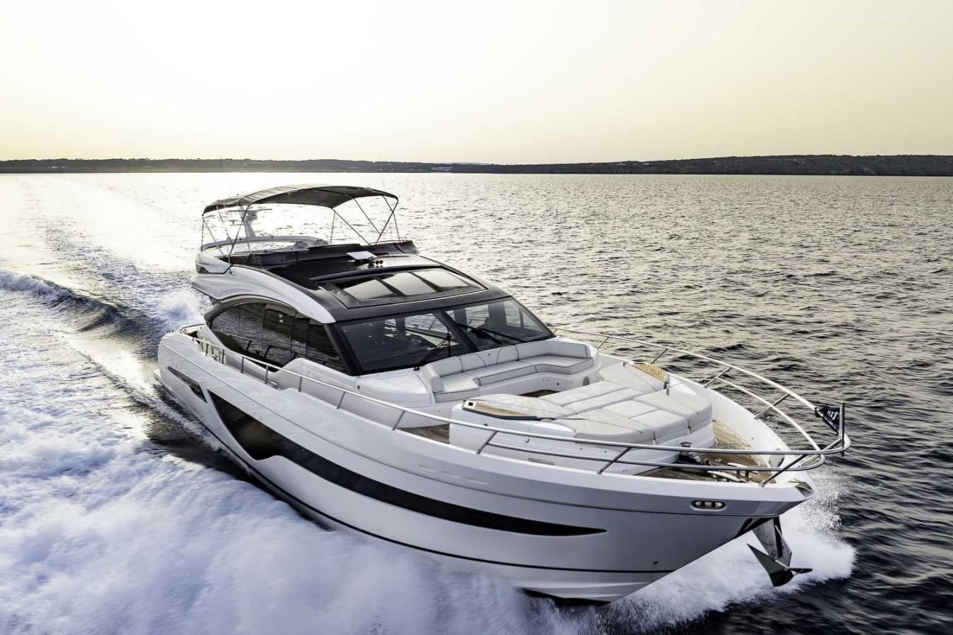 Modern white Why Knot Yacht speeds across open water, leaving a foamy wake with a distant shoreline visible.