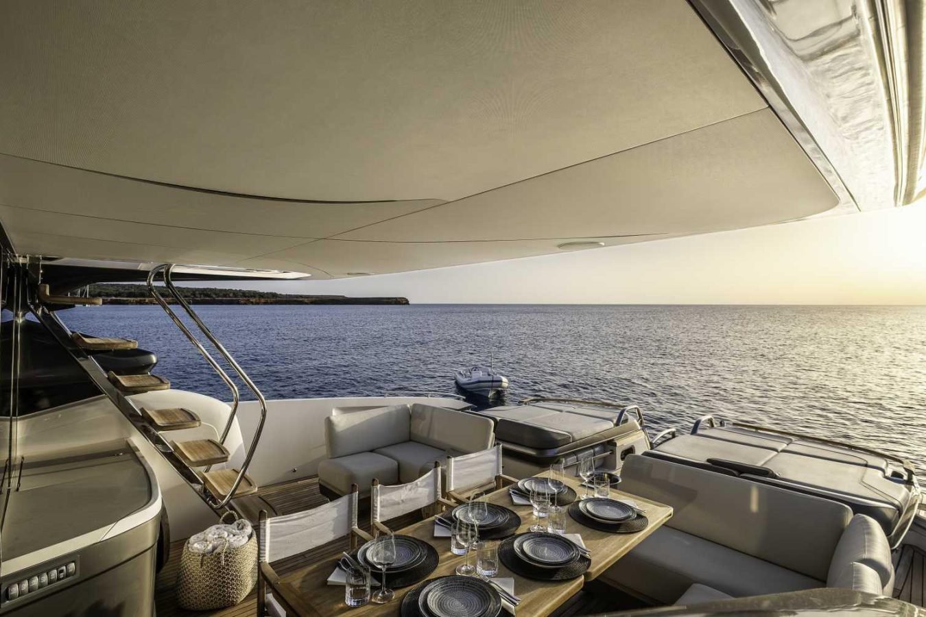 Elegant Princess S78 yacht deck at sunset with plush seating, set dining table, and ocean view; small boat nearby.