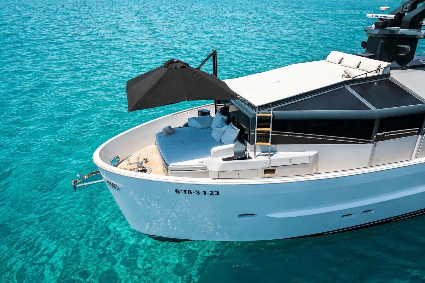 The Arcadia 85 yacht for charter boasts a sunbed on deck, floating on clear turquoise water under a bright sky.