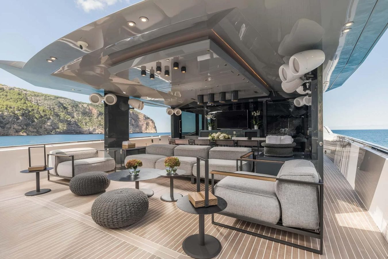 Luxury yacht deck on Dhamma II with modern gray sofas, tables, and plants; Arcadia 85 yacht for charter with ocean views.