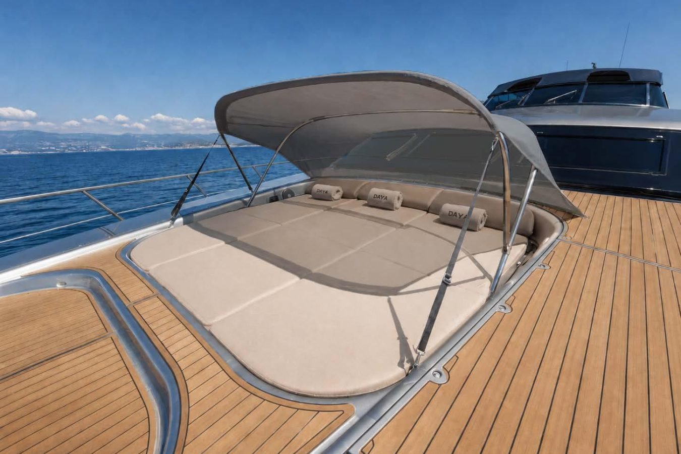 Large sunbed with canopy on Mangusta 105 yacht for charter, calm blue sea, clear sky, and distant shoreline.