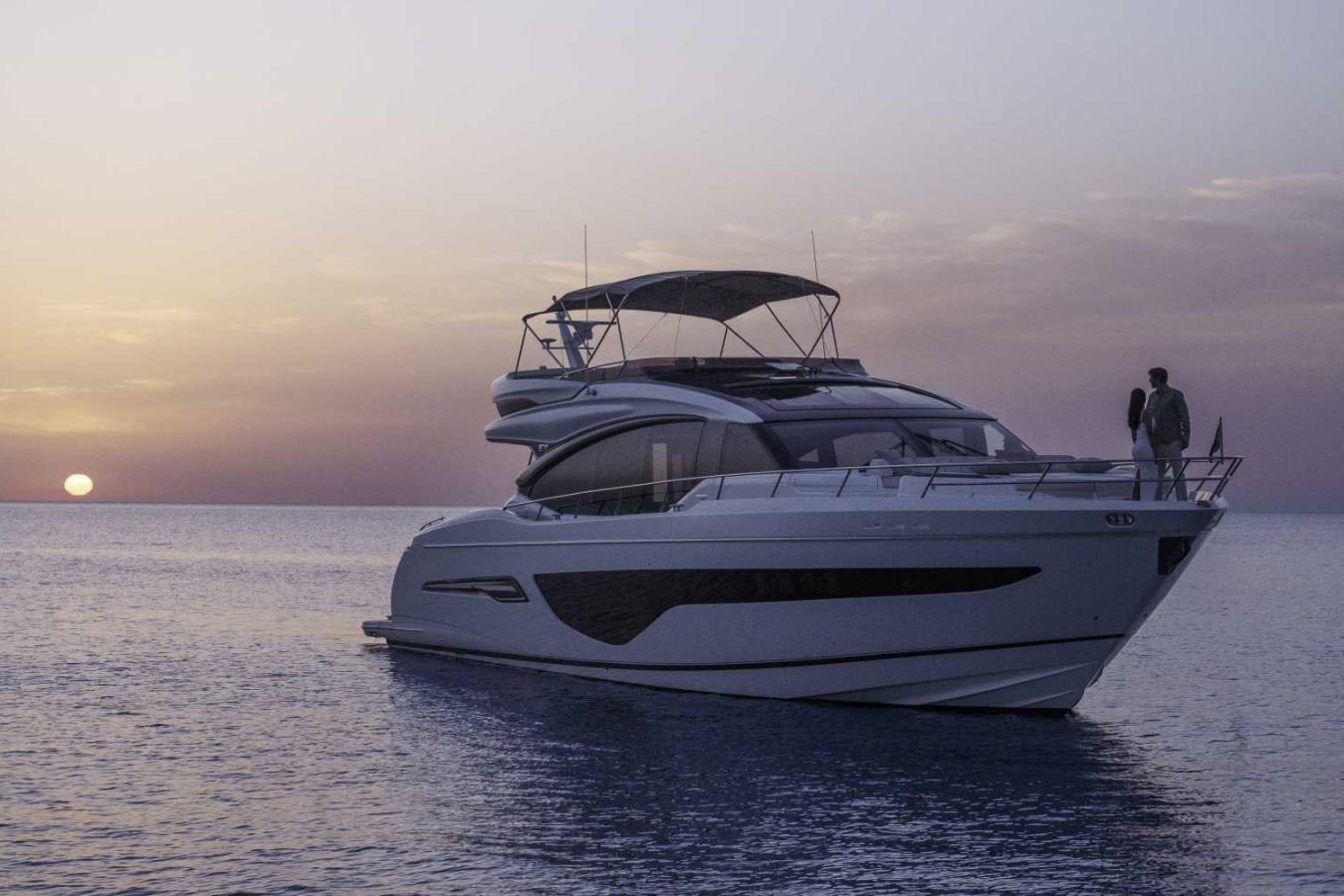 A modern Princess S78 floats on calm water at sunset; two people on deck admire the view aboard this yacht for charter.