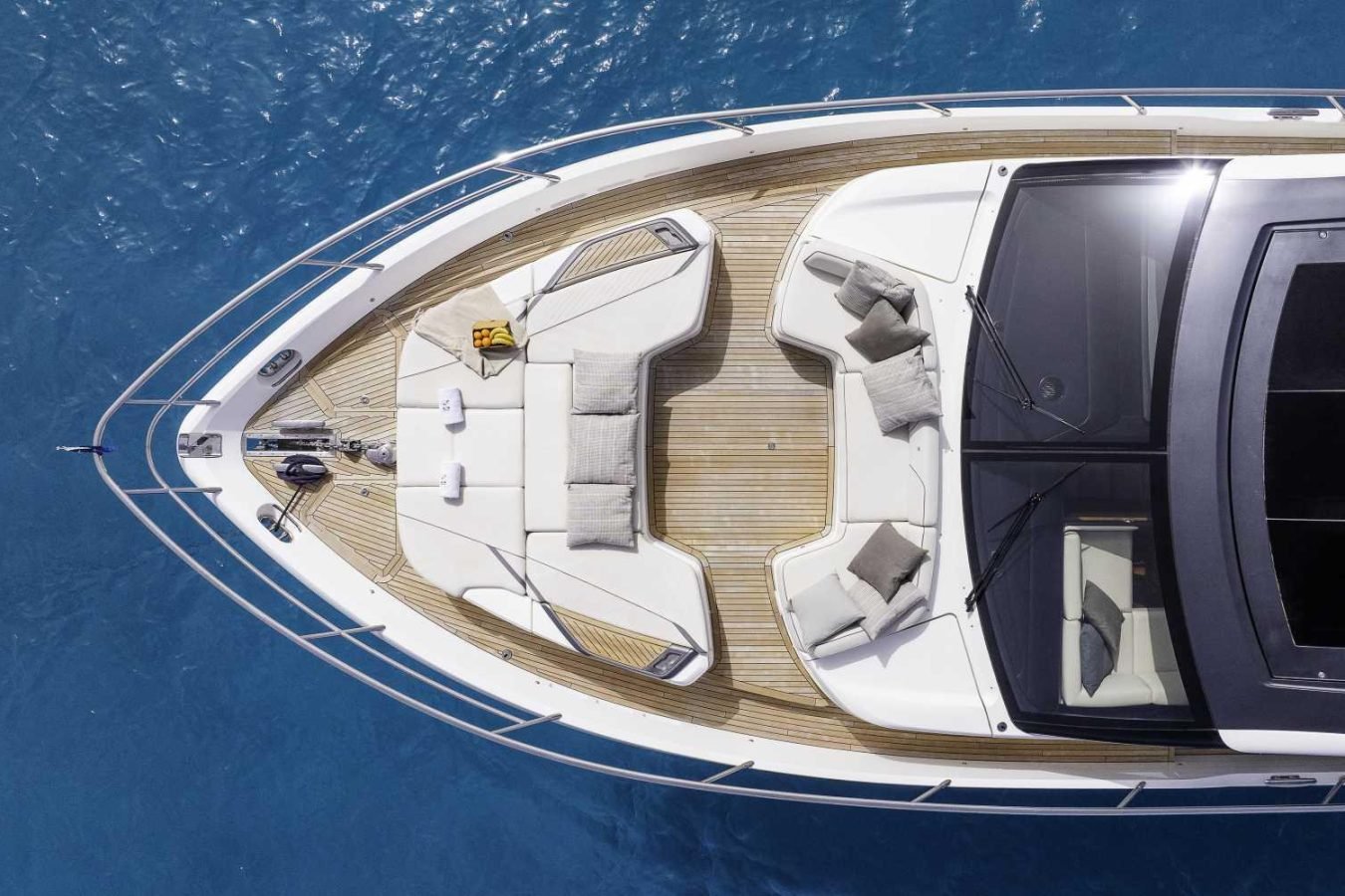 A Princess S78 yacht’s bow deck with cushioned seating, pillows, and table floats on clear blue water.