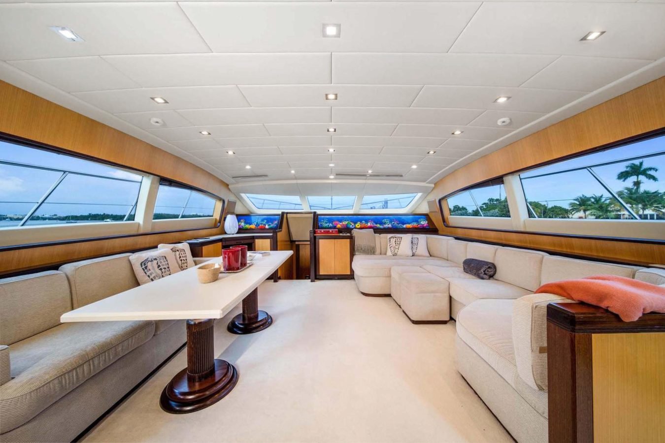 Modern Mangusta 105 yacht interior with cream sofas, a white table, large windows, and scenic water views outside.