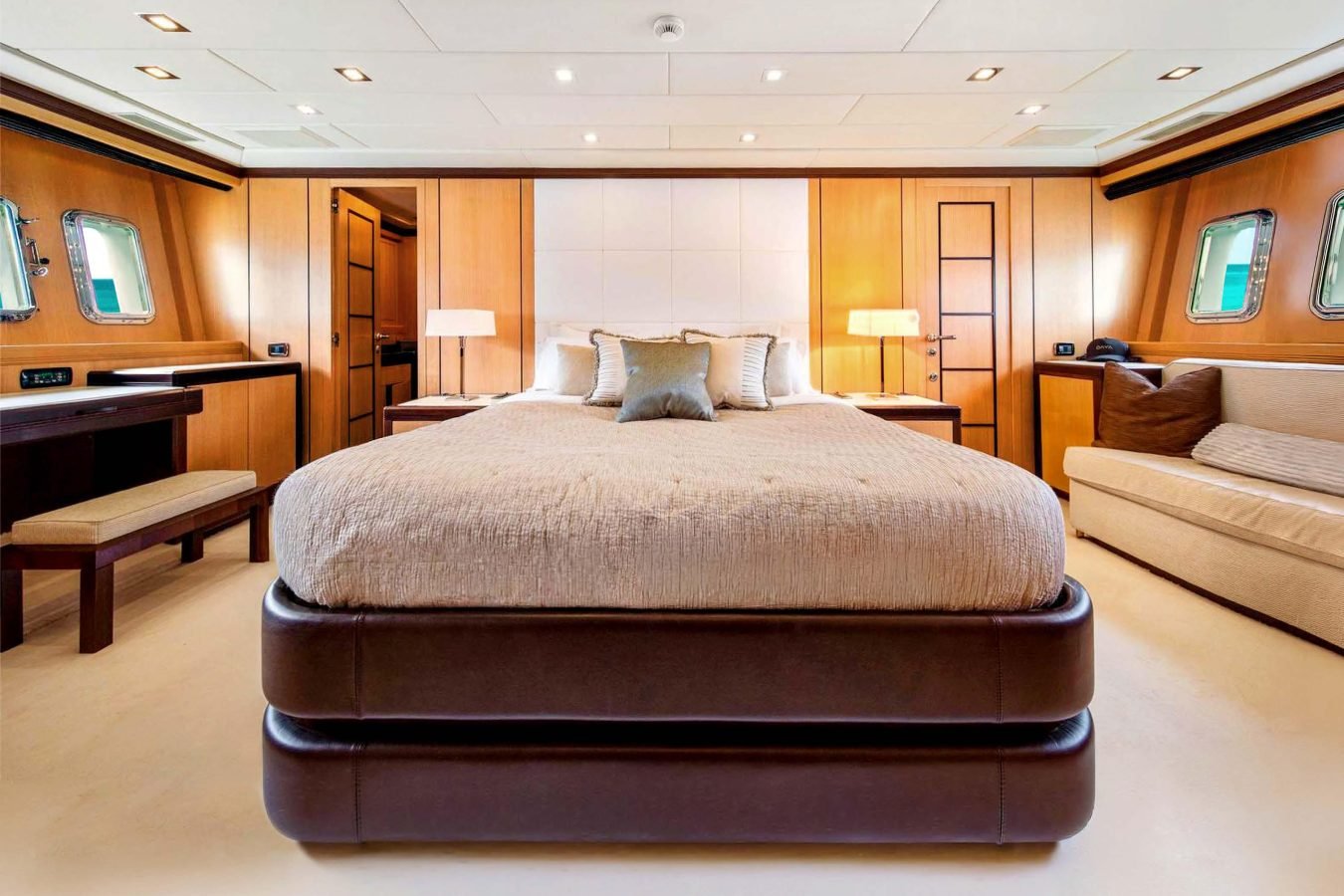 Luxurious Mangusta 105 bedroom with tan bedding, wood-paneled walls, sofa, desk, lamps, and porthole windows.