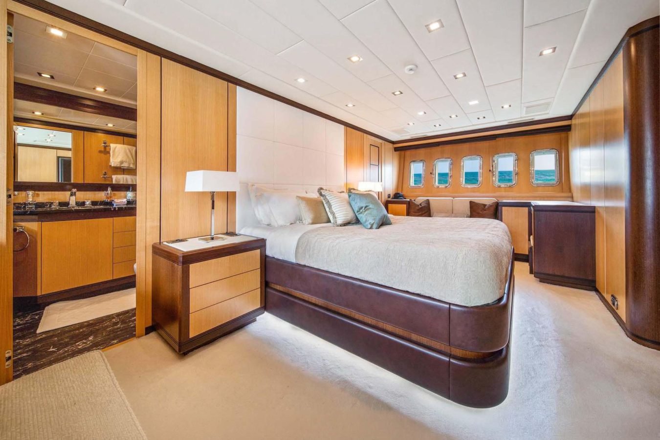 Luxurious Mangusta 105 yacht bedroom with large bed, wood decor, porthole windows—perfect for your Daya yacht charter.