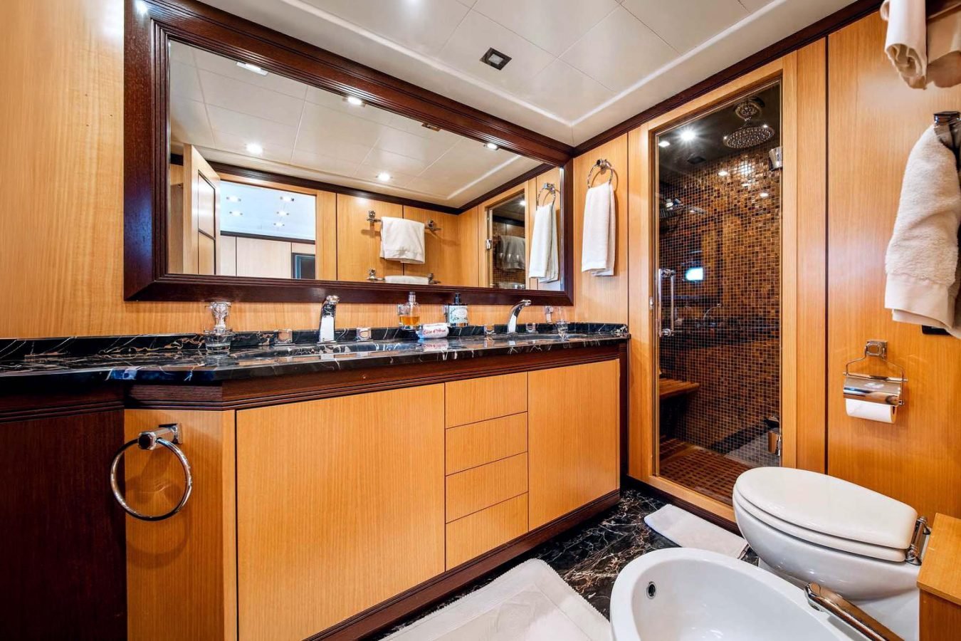 Modern bathroom on Mangusta 105 yacht charter with wood cabinets, marble counter, glass shower, and bidet.