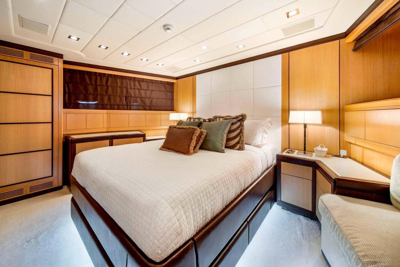 Modern bedroom with wood panel walls, large bed, and soft lighting—luxury like a Mangusta 105 yacht for charter.