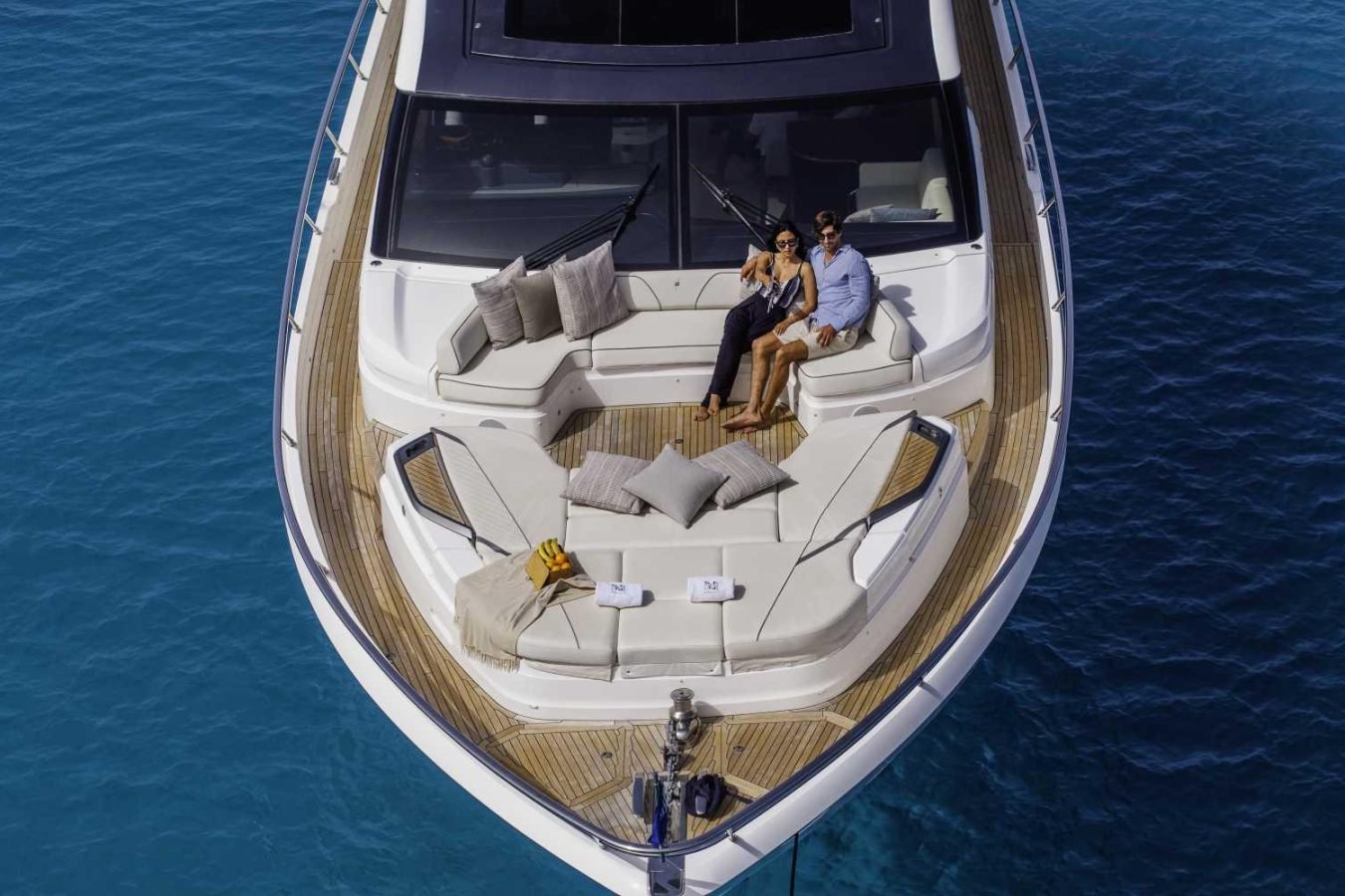 A couple relaxes on the cushioned deck of the Princess S78, surrounded by blue water under a clear sky.