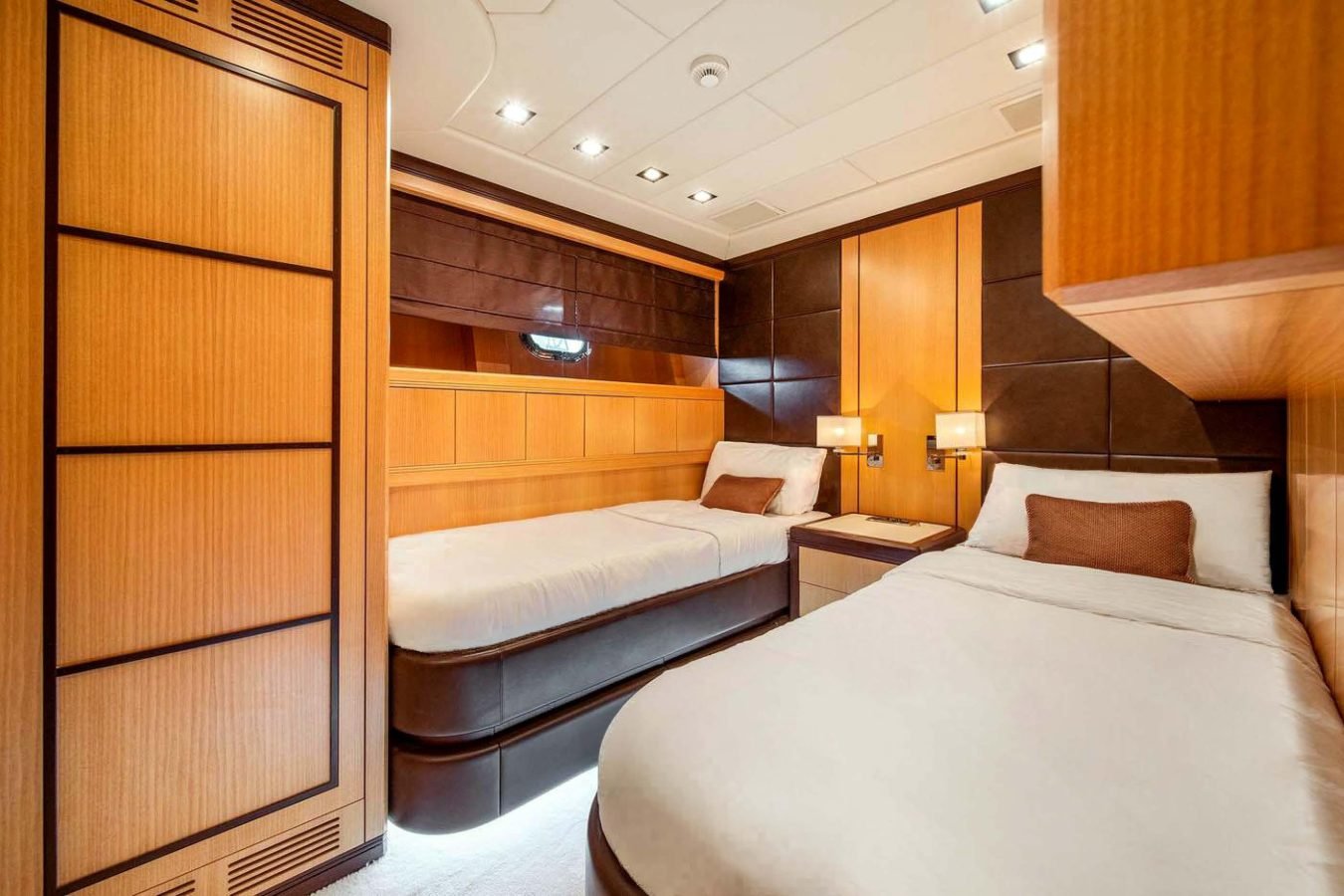 Two single beds in a modern room with wood paneling aboard the Mangusta 105 yacht for charter, featuring soft lighting.