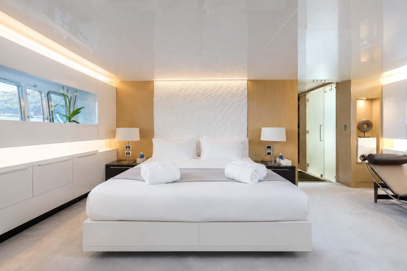 Modern Arcadia 85 yacht bedroom with white bed, wood accents, glass shower, and ocean view window—ideal yacht for charter.