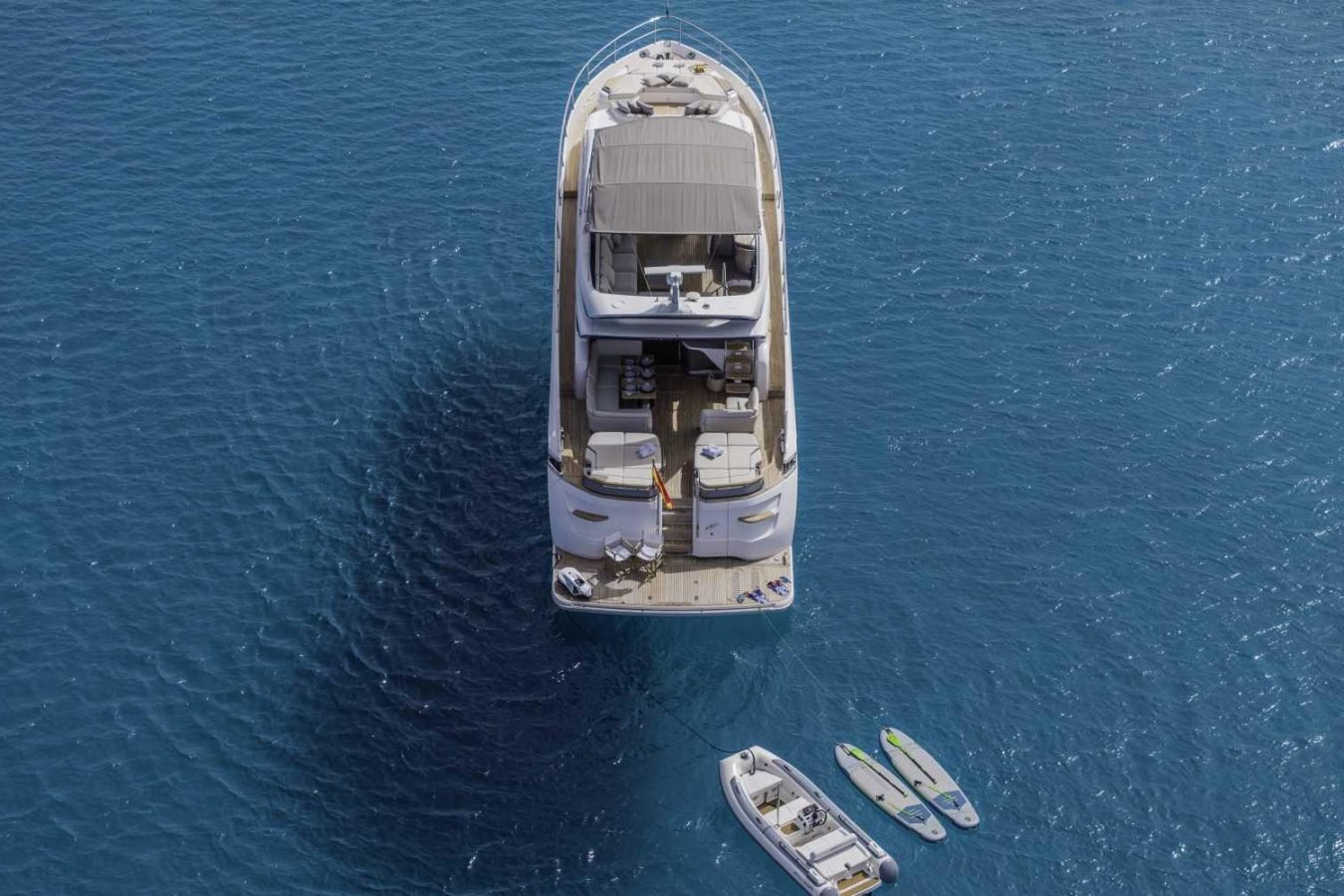 A large Princess S78 yacht for charter on blue water, viewed from above, with small boats and paddleboards nearby.