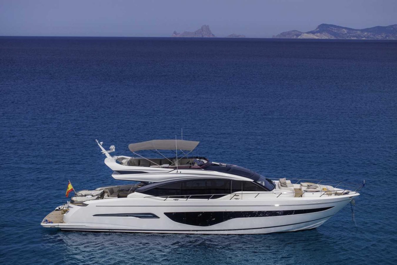 The Princess S78 yacht floats on calm blue water with distant mountains, promising a luxurious escape under a clear sky.