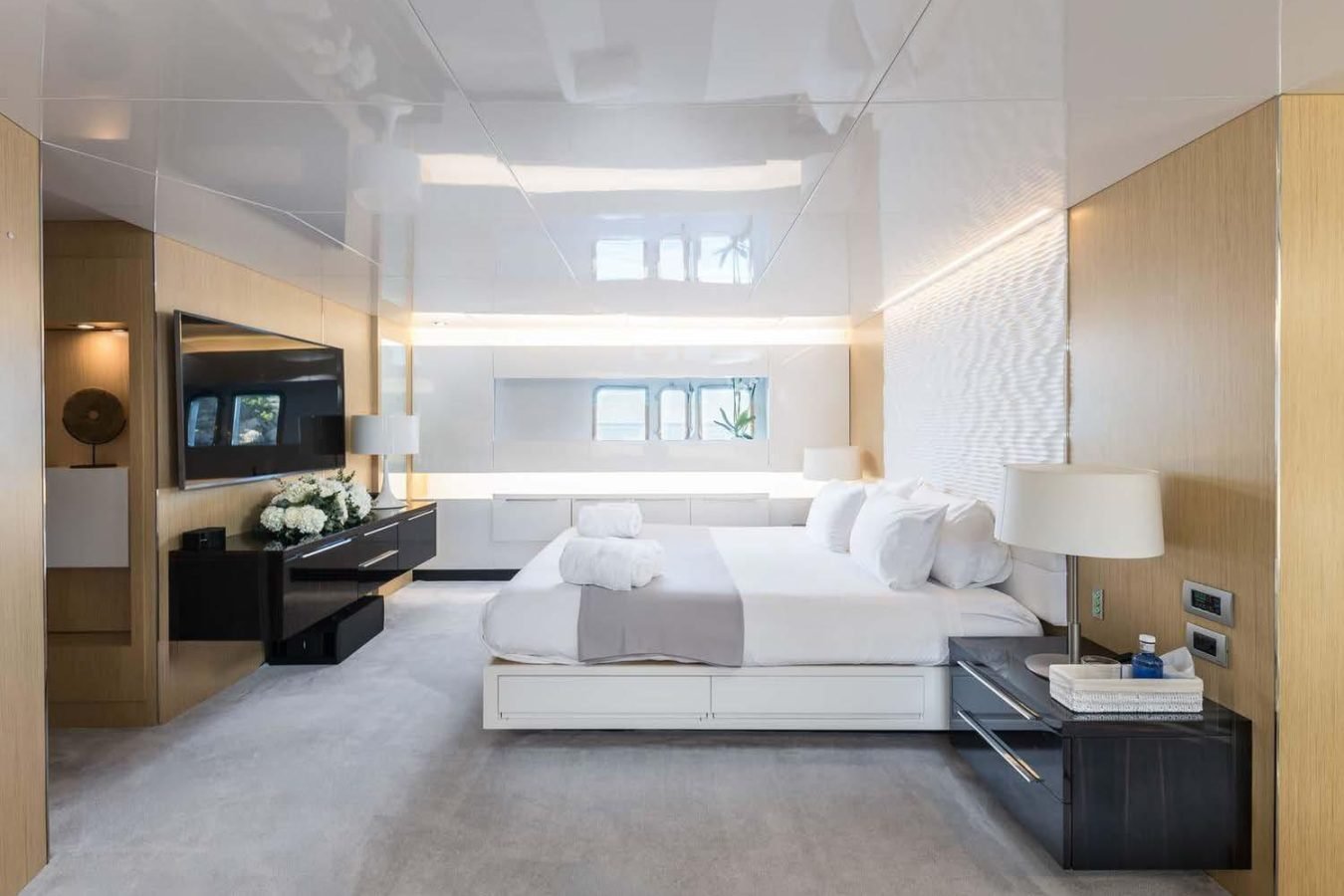 Modern Arcadia 85 yacht bedroom with large bed, TV, white decor, flowers, lamps, and bright natural light.
