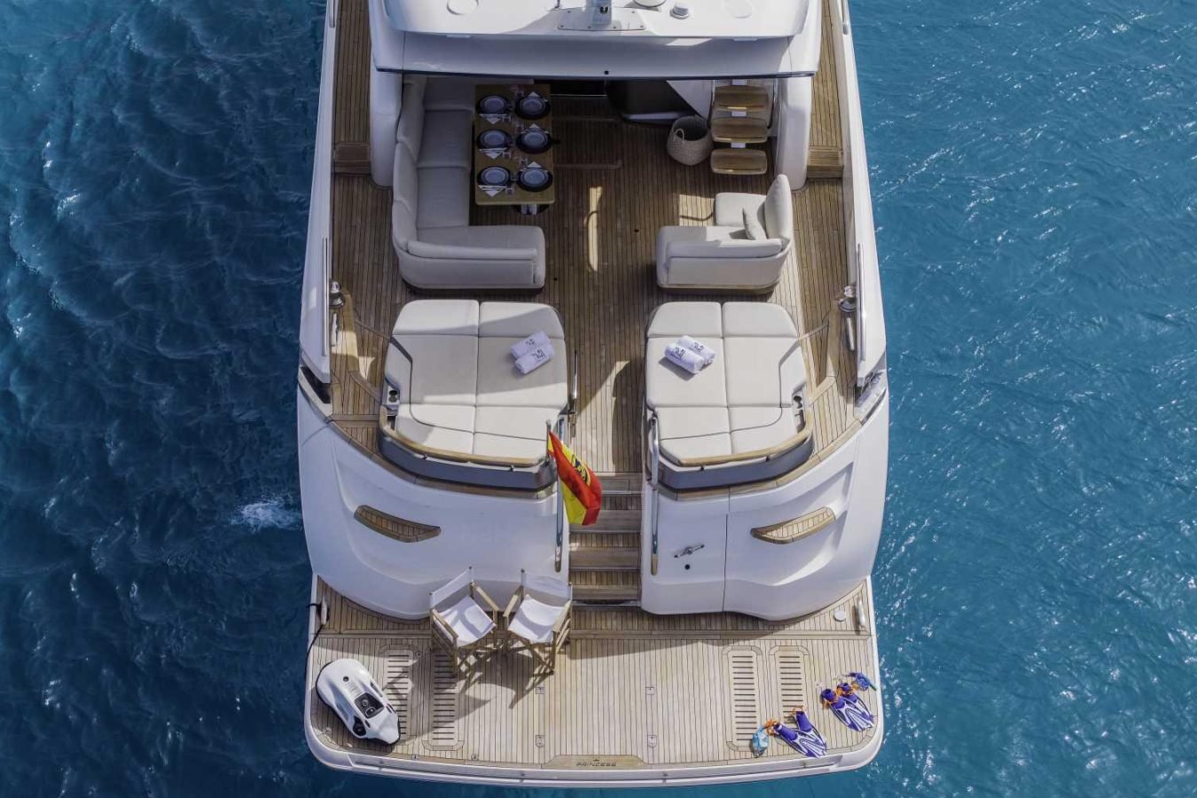 Aerial view of Princess S78 yacht for charter, with lounge chairs, dining table, flag, and a small boat at the back.