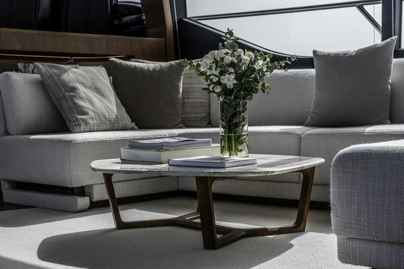 Marble coffee table with books, flower vase, and sofas in a sunlit living room aboard the Princess S78 yacht for charter.