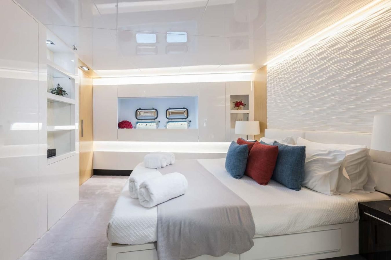 Modern bedroom aboard Arcadia 85: large bed, white linens, blue and red pillows, shelves, and two small windows.