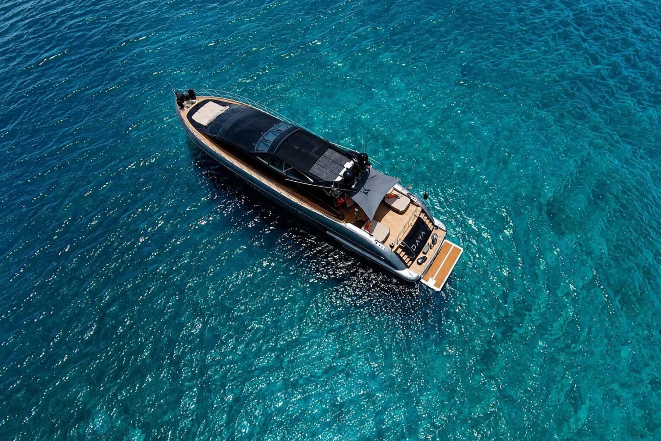 A sleek Mangusta 105 yacht floats on vibrant blue water, viewed from above—a perfect yacht for charter moments.