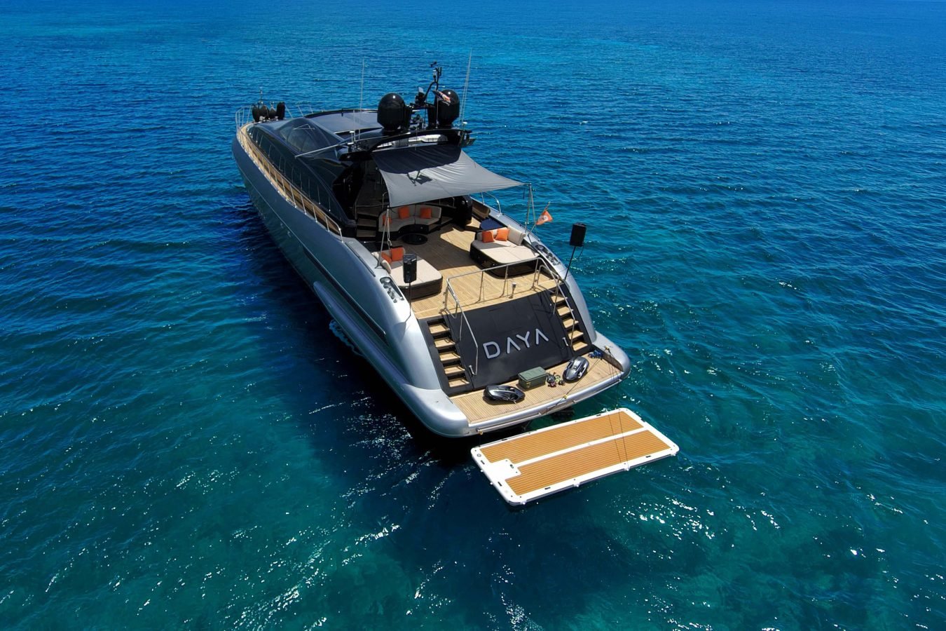 The Daya Yacht, a stunning Mangusta 105, is anchored in clear blue sea with its swim platform extended at the stern.