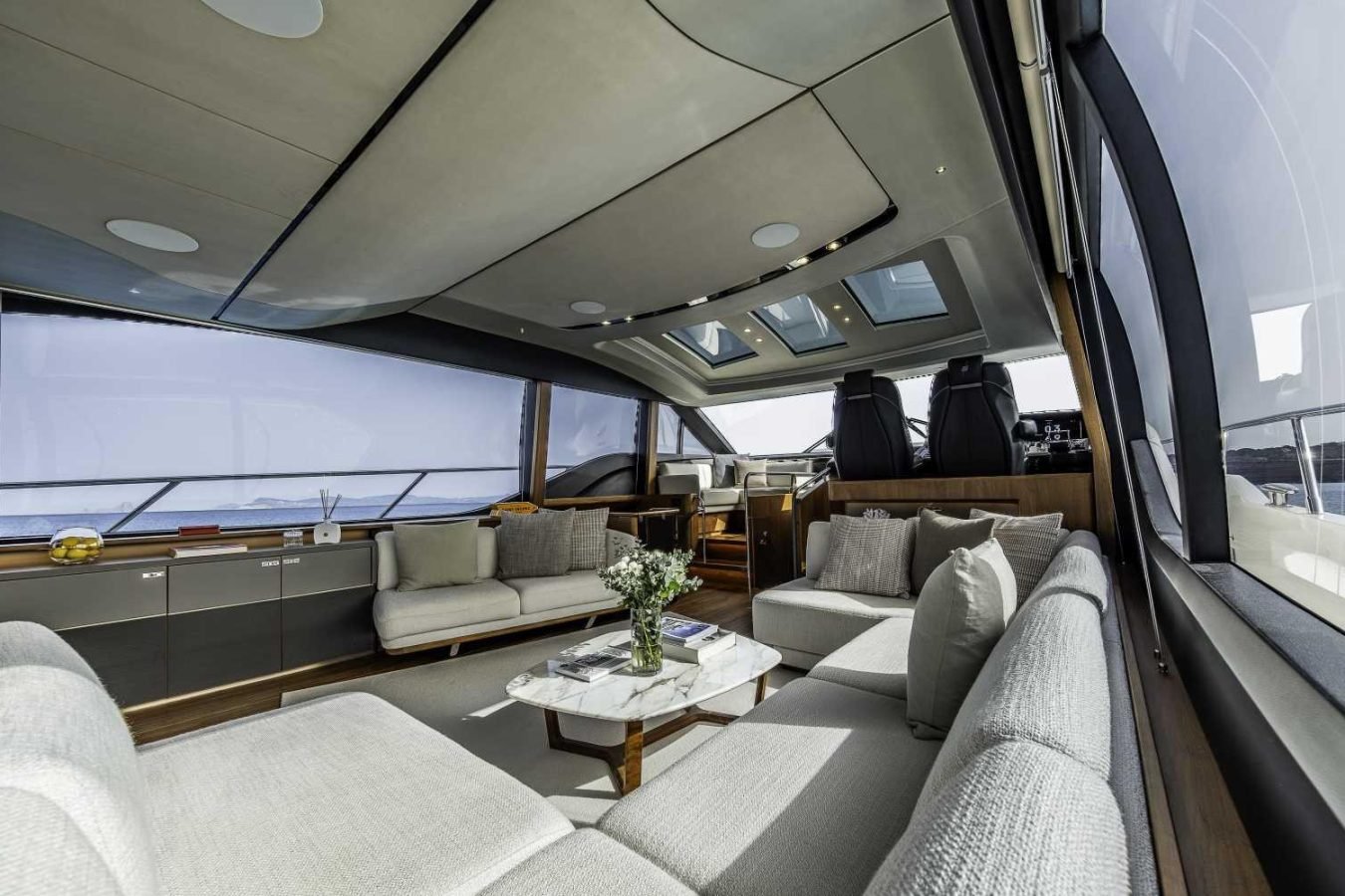Modern Princess S78 yacht interior with large windows, light gray sofas, a marble coffee table, and water views.
