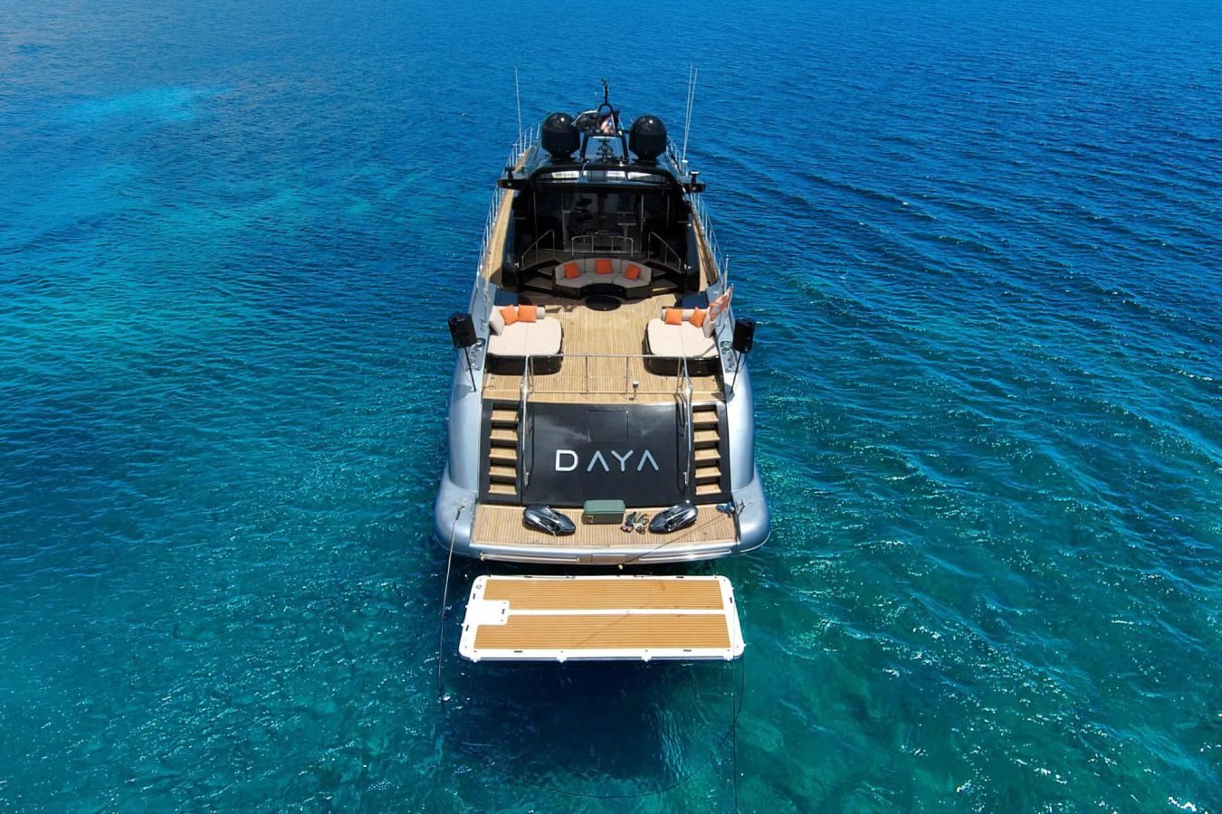 The Daya Yacht, a Mangusta 105 yacht for charter, floats on clear blue water with its swim platform extended at the stern.