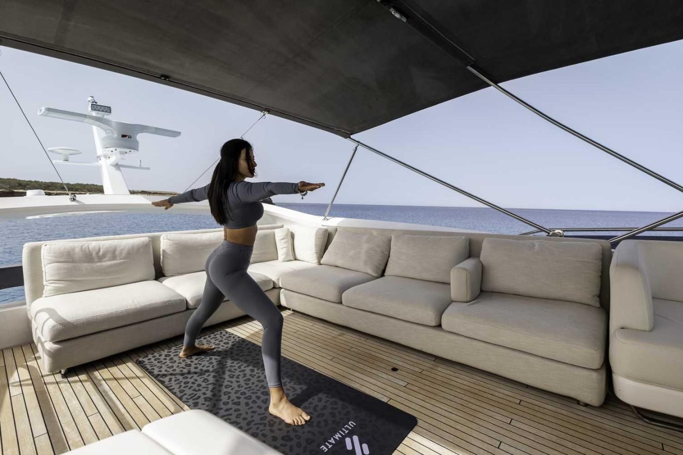 Woman practices yoga on a Why Knot Princess S78 yacht for charter, standing on a mat facing the sea under a canopy.