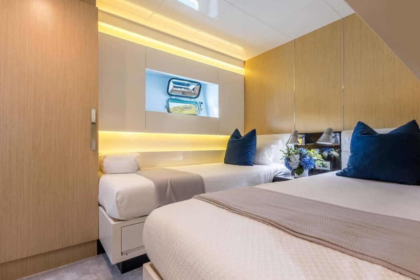 Modern yacht bedroom on Arcadia 85 with twin beds, blue pillows, wood paneling, and flowers—Dhamma II yacht for charter.