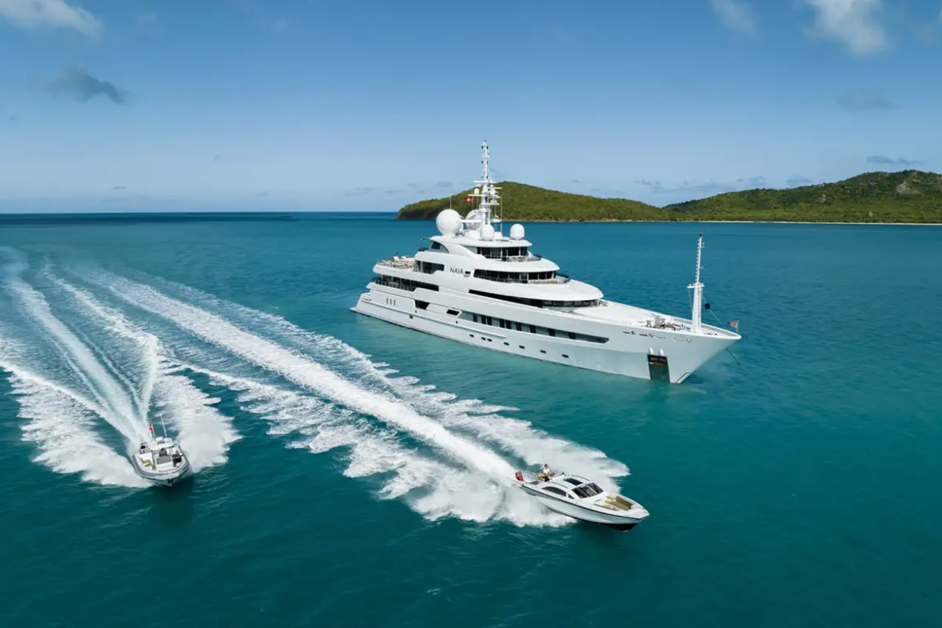 The Freire Naia Yacht for Charter sits in blue water, speedboats passing by, framed by green hills in the background.