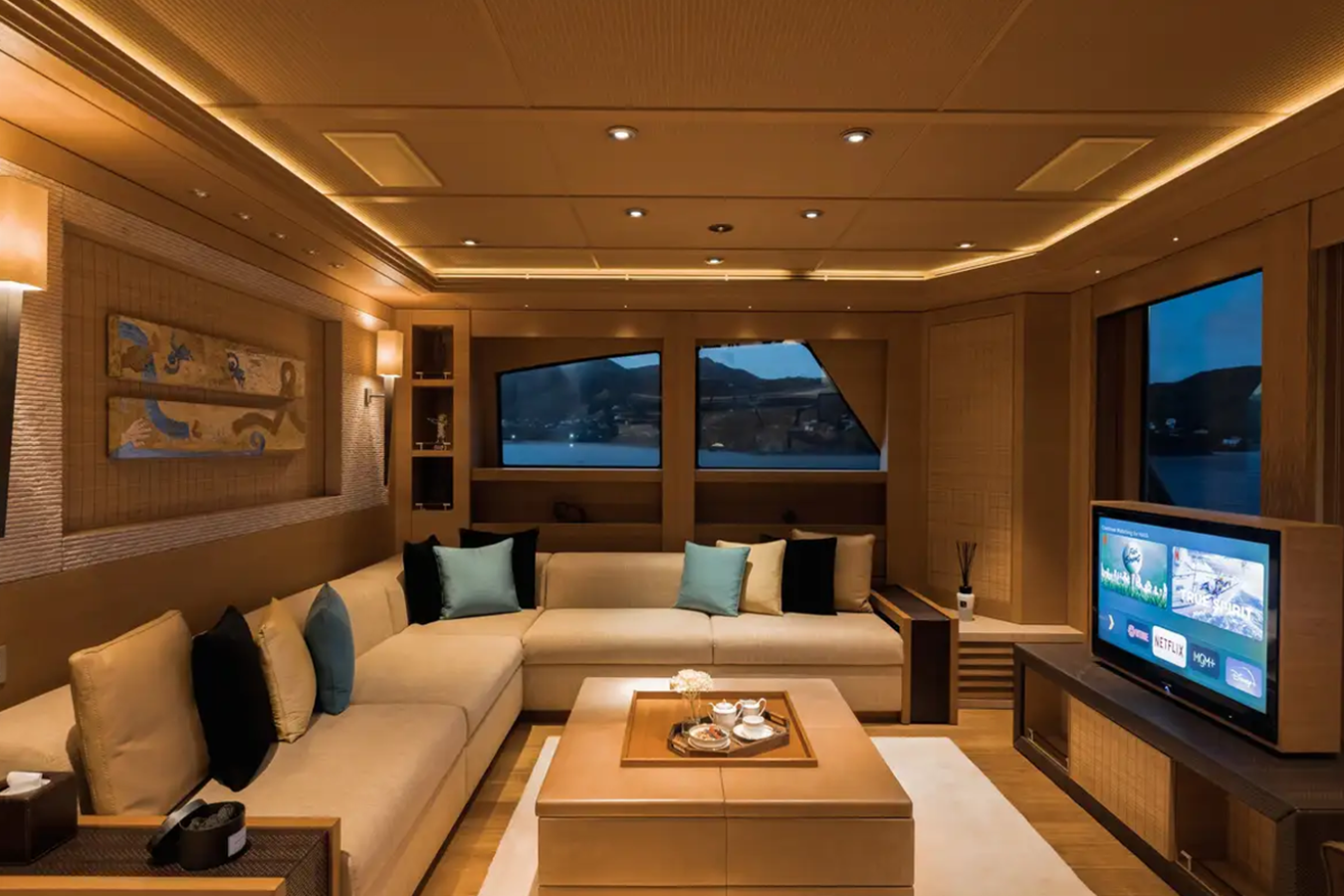 Modern yacht lounge with beige sofas, TV, large windows, and soft lighting aboard the Freire Naia Yacht for Charter.