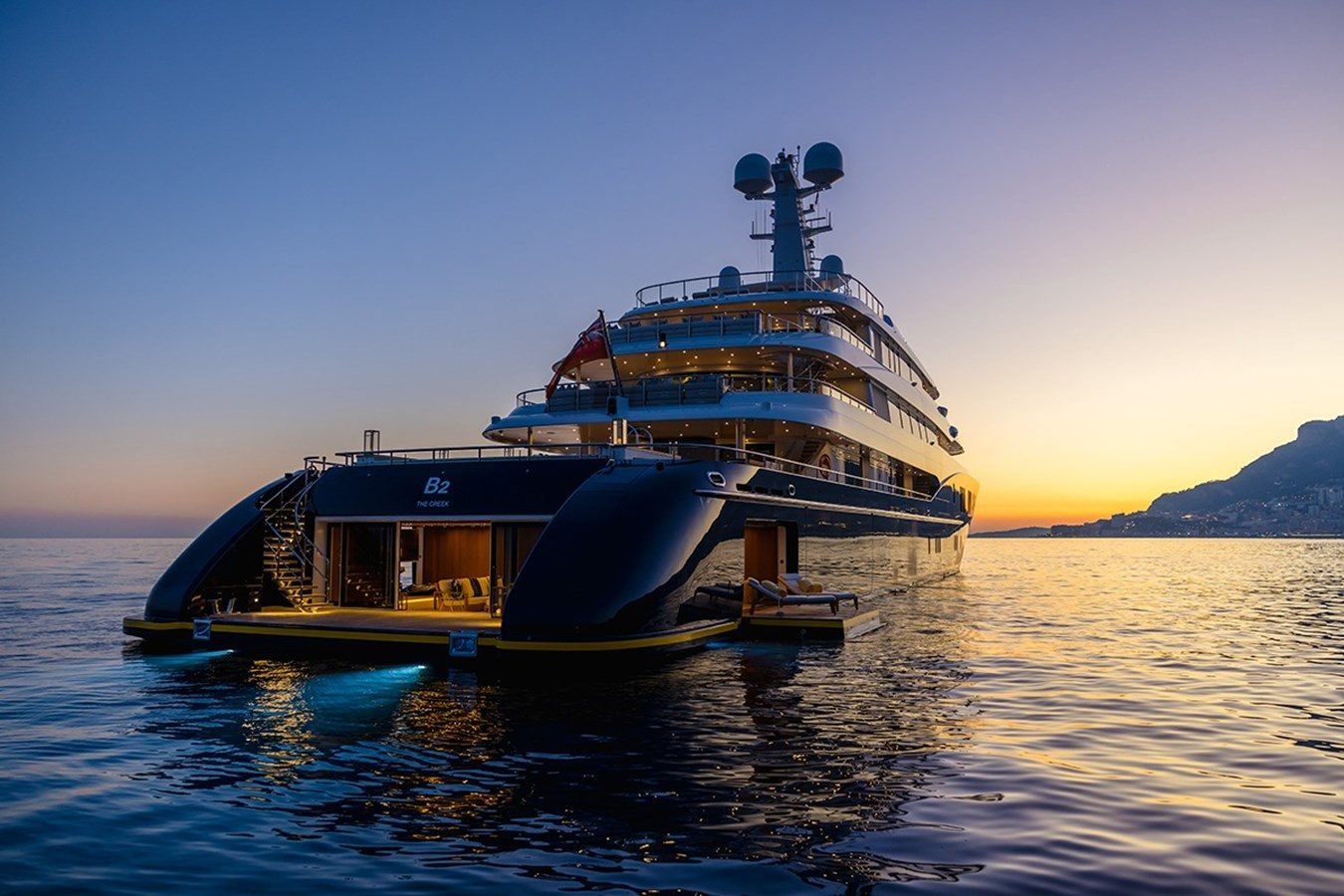 Abeking & Rasmussen HBC Yacht for Charter on calm water at sunset, open deck and lounge, mountains in the background.