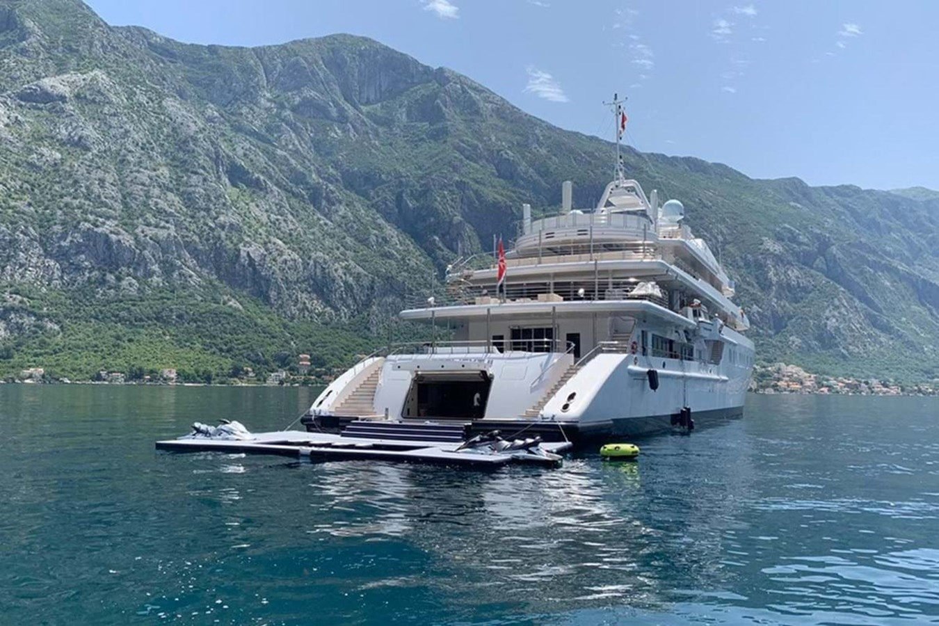 The Neorion Moonlight II Yacht for Charter is anchored near green slopes, with jet skis and a floating dock on calm water.