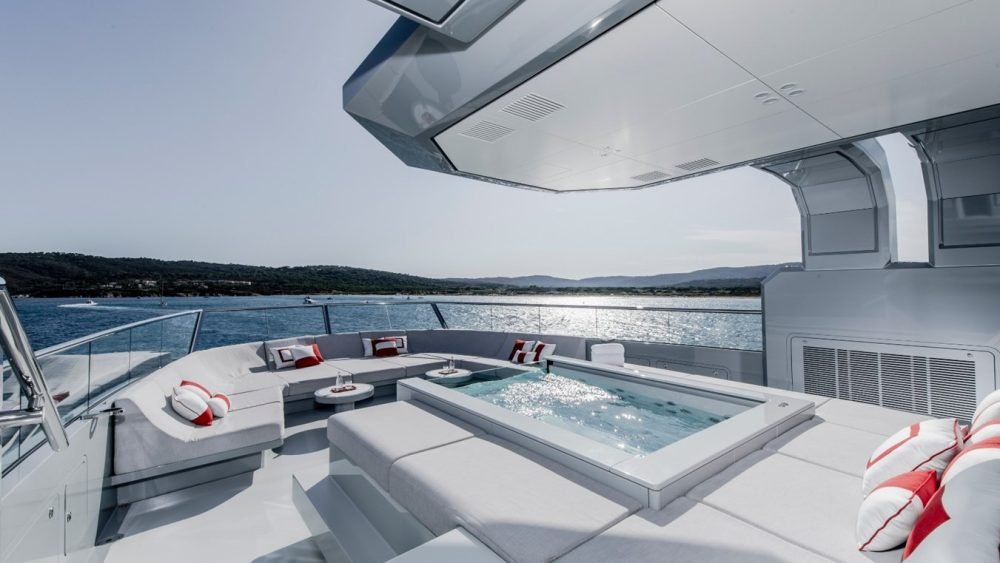 Luxury Silver Yachts Bold Yacht for Charter: deck with jacuzzi, gray seating, red-white pillows, scenic ocean views.