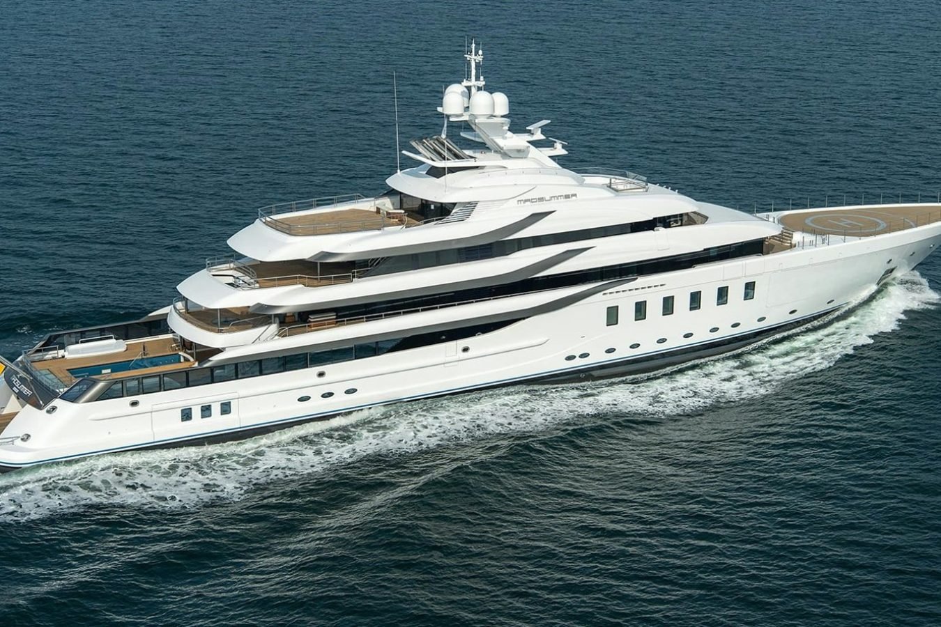 The Lurssen CC-Summer Yacht for Charter, a large white luxury vessel, glides on calm blue ocean waters with a graceful wake.